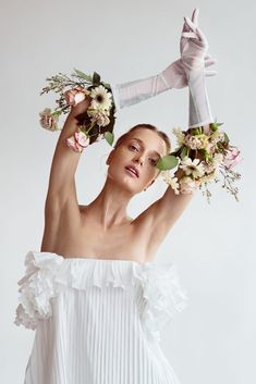 a woman in white dress holding flowers up to her head