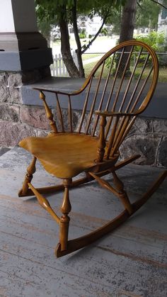 a wooden rocking chair sitting on top of a stone floor next to a tree in front of a building