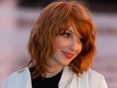 a close up of a person wearing a white jacket and black shirt with red hair