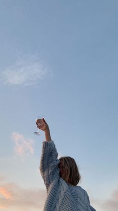 a woman holding a wine glass up in the air while standing on a beach at sunset