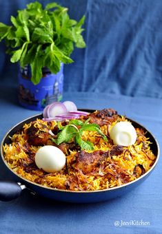 a pan filled with rice and vegetables next to a potted plant on a blue table cloth