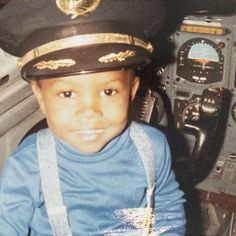 a young boy wearing a pilot's hat sitting in the cockpit of a plane