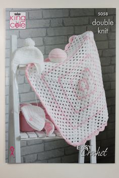 a crocheted baby blanket and hat sitting on top of a white shelf next to a brick wall