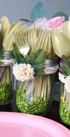 mason jars filled with flowers and spoons on top of a pink plate next to plates