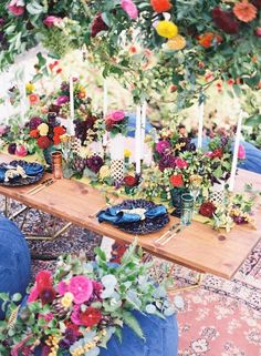 the table is set with flowers and candles for an outdoor dinner or party, it's surrounded by greenery