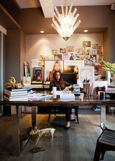 a woman sitting at a desk in front of a chandelier with pictures on the wall