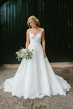 a woman standing in front of a barn wearing a wedding dress