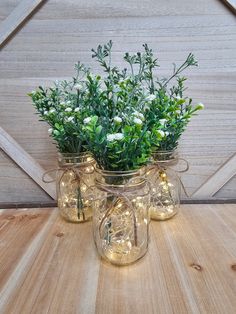 three mason jars filled with white flowers sitting on top of a wooden table