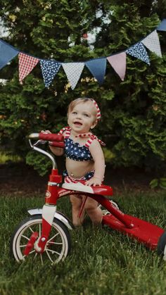 a small child riding a red tricycle in the grass with bunting on it's head