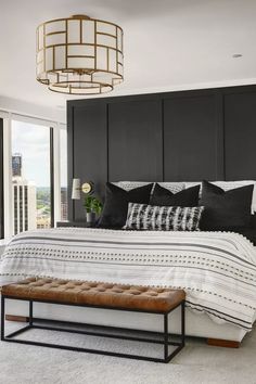 a bedroom with black and white bedding, a bench, and a large window