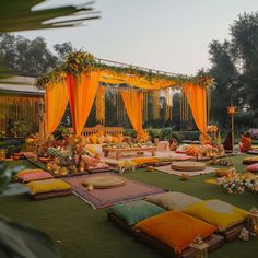 an outdoor wedding setup with yellow draping and orange pillows on the ground, surrounded by greenery