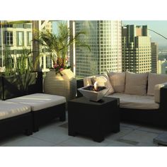 a living room with couches and tables on top of a roof in front of tall buildings