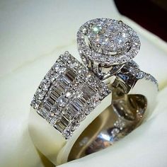 two diamond rings sitting on top of a white cloth covered ring box, with the center surrounded by smaller diamonds