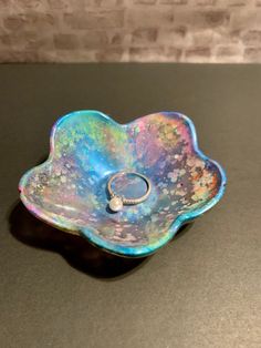 a ring sits in the middle of a colorful flower shaped dish on a black surface