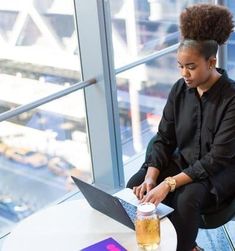 a woman sitting at a table with a laptop computer on her lap and a drink in front of her