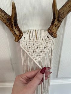 a hand holding a white macrame with antlers on it's head