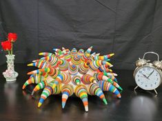 a clock, vase with flowers and an animal made out of pencils on a table