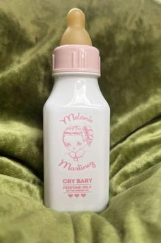 a baby bottle sitting on top of a green bed sheet with a pink cap and handle