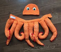 an octopus made out of orange fabric on a wooden floor with eyes and nose sticking out