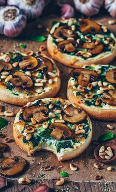 small pizzas with mushrooms, spinach and pine nuts on a wooden table next to garlic cloves