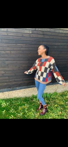 a woman standing in the grass with her arms spread out, wearing a sweater and leggings