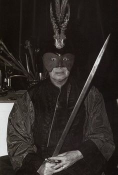 a man wearing a mask and holding a large knife in his right hand while sitting on a chair