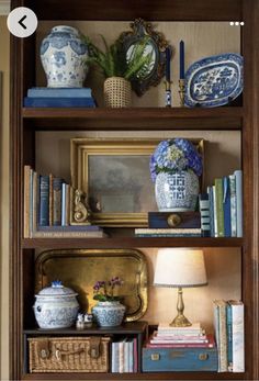 a bookshelf with blue and white vases on it's shelves next to a lamp