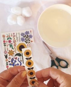 someone is cutting up some stickers on a table with scissors and flowers in front of them