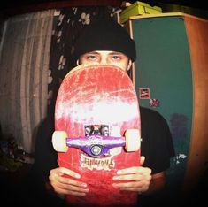 a man holding a skateboard in front of his face while wearing a beanie