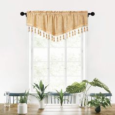 a wooden table topped with potted plants next to a large window covered in curtains