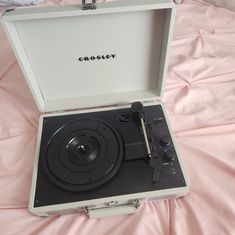 an open record player sitting on top of a pink sheet covered bed in a suitcase