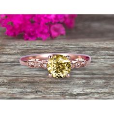 a yellow diamond ring sitting on top of a wooden table with pink flowers in the background