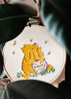 a close up of a embroidery on a plant with a teddy bear holding a basket