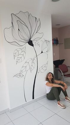 a woman sitting on the floor in front of a wall with flowers painted on it