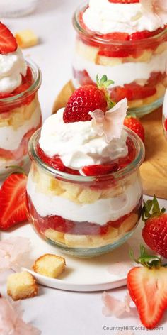 strawberry shortcakes in small glass jars with whipped cream and strawberries on the side