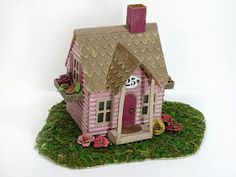 a pink doll house sitting on top of a green patch of grass next to a white wall