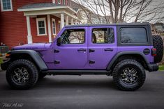 a purple jeep is parked in front of a red house with two large tires on it