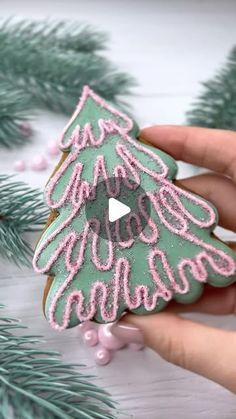 someone is holding a decorated cookie in front of some christmas tree decorations and pine branches