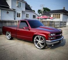 a red pick up truck parked in front of a house with white rims on it