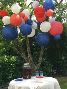 a table topped with red, white and blue paper lanterns next to a small tree