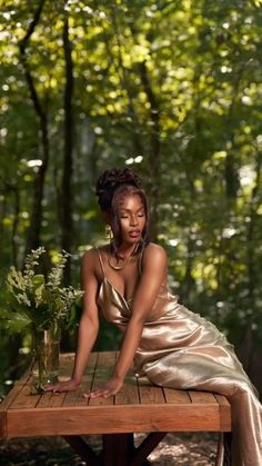 a woman is sitting on a wooden table in the middle of a forest with flowers