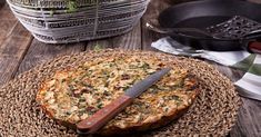 a pizza sitting on top of a wicker plate next to a knife and potted plant