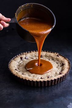 someone pouring caramel sauce on top of a cookie