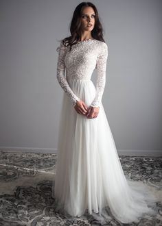 a woman in a long sleeved wedding dress posing for the camera with her hands on her hips