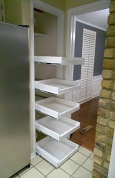 an empty pantry with white shelves next to a brick wall and tiled floor in a kitchen