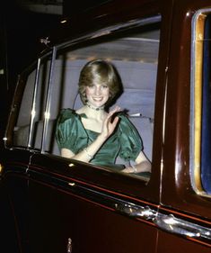 a woman sitting in the passenger seat of an old car waving at someone out the window