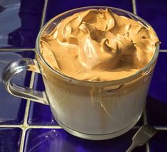 a glass mug filled with whipped cream sitting on top of a blue tile countertop