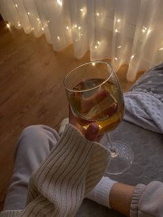 a person holding a glass of wine in front of a window with lights on it