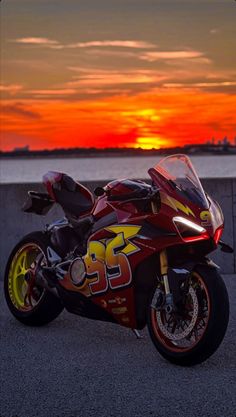 a red motorcycle parked on the side of a road near the ocean at sunset or dawn