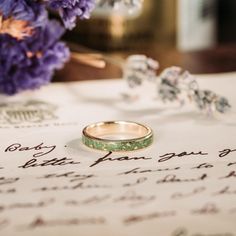 two wedding rings sitting on top of a piece of paper next to some purple flowers